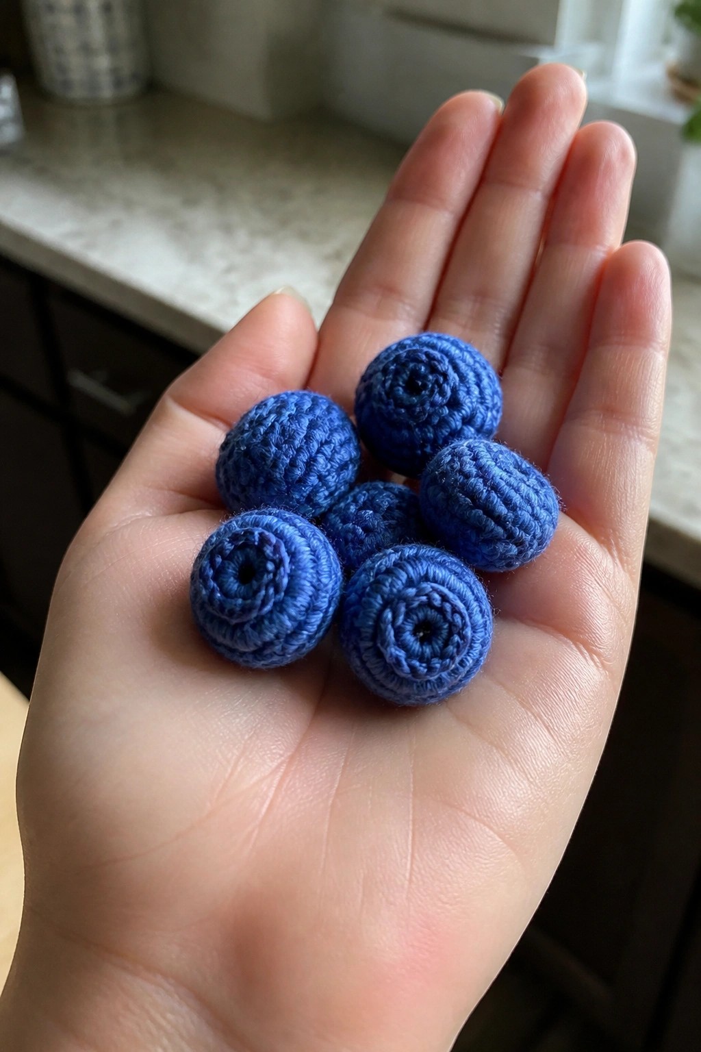 Open hand holding multiple small blue crocheted spheres with spiral patterns.