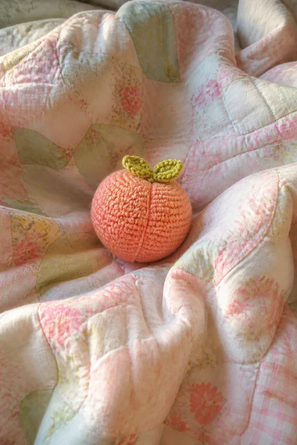 Crocheted peach with green leaves on pink floral patchwork quilt