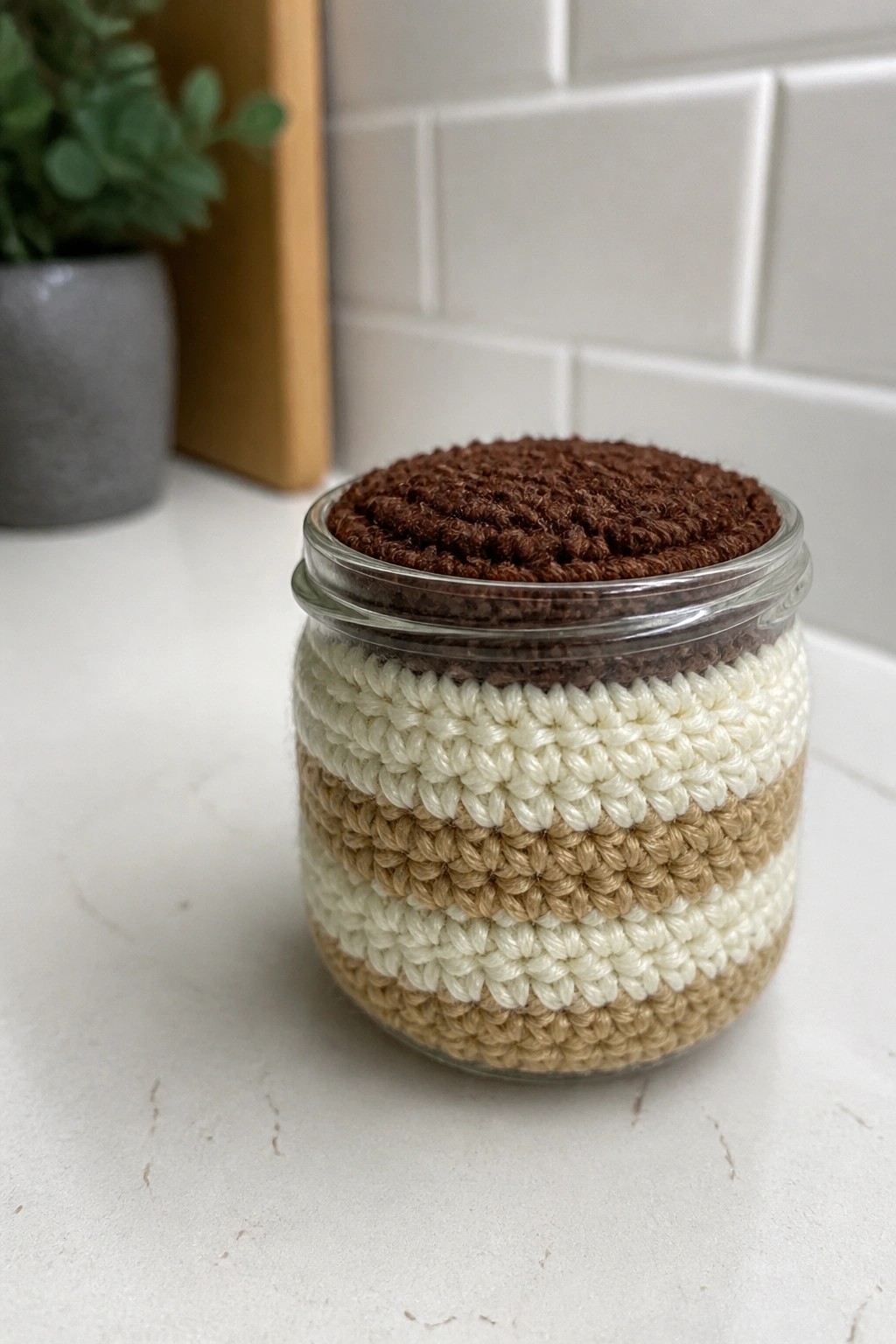 Glass jar with striped beige-white crocheted cover and brown textured top on counter