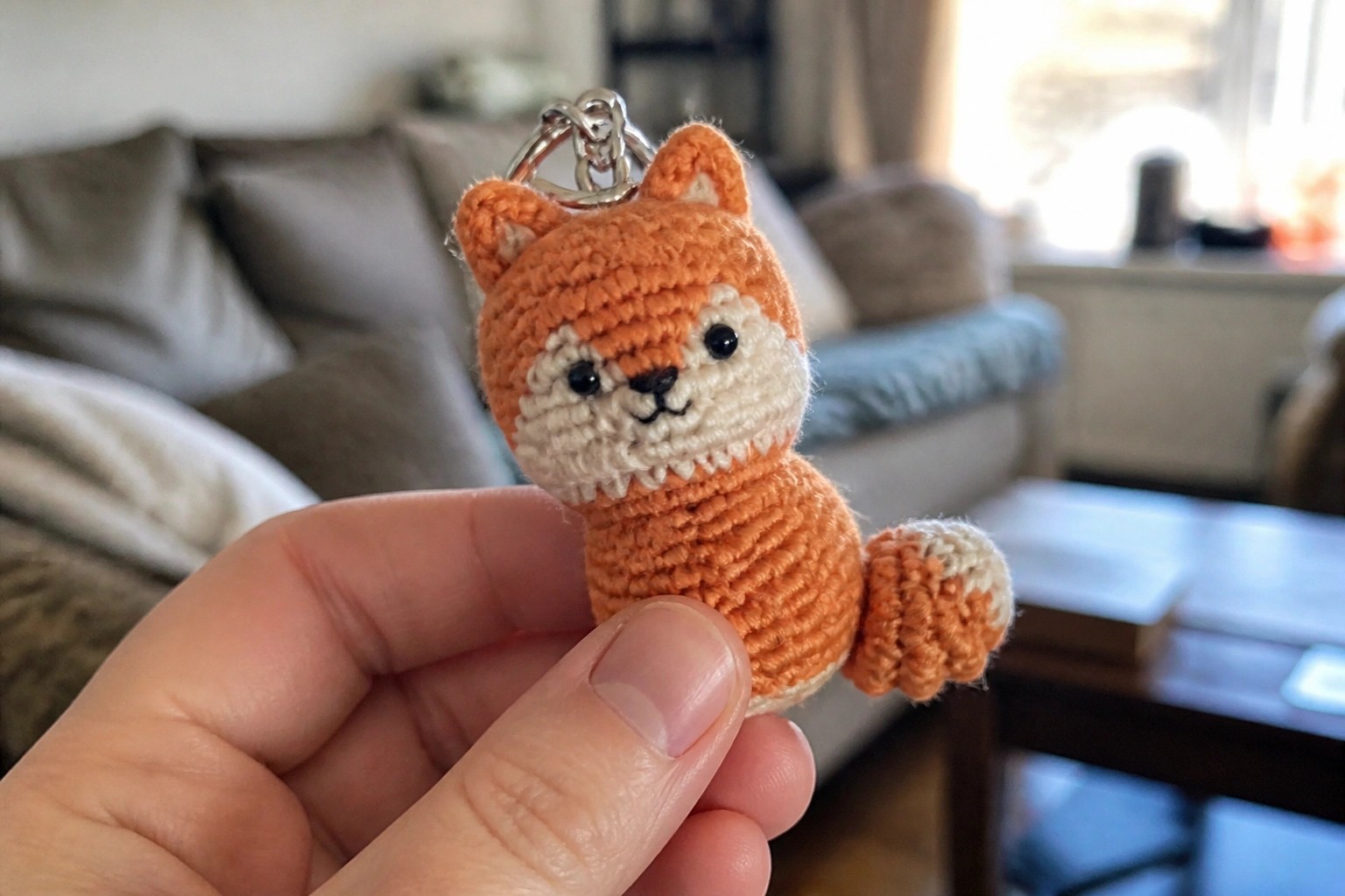 Hand holding small orange crocheted fox keychain with white ears and tail tip
