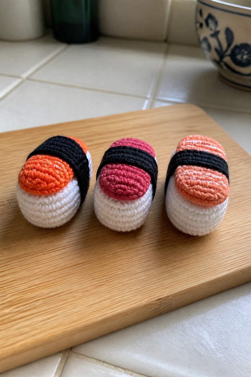 Three crocheted sushi nigiri with white bases and colorful tops on wooden board.
