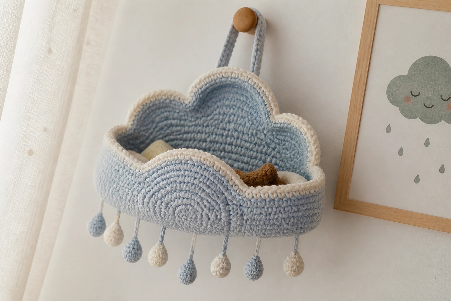 Light blue crocheted cloud basket with dangling pom-poms on wooden hook