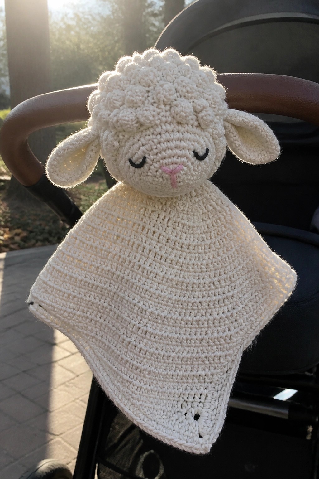White crocheted lamb with closed eyes on square blanket over stroller in sunlight
