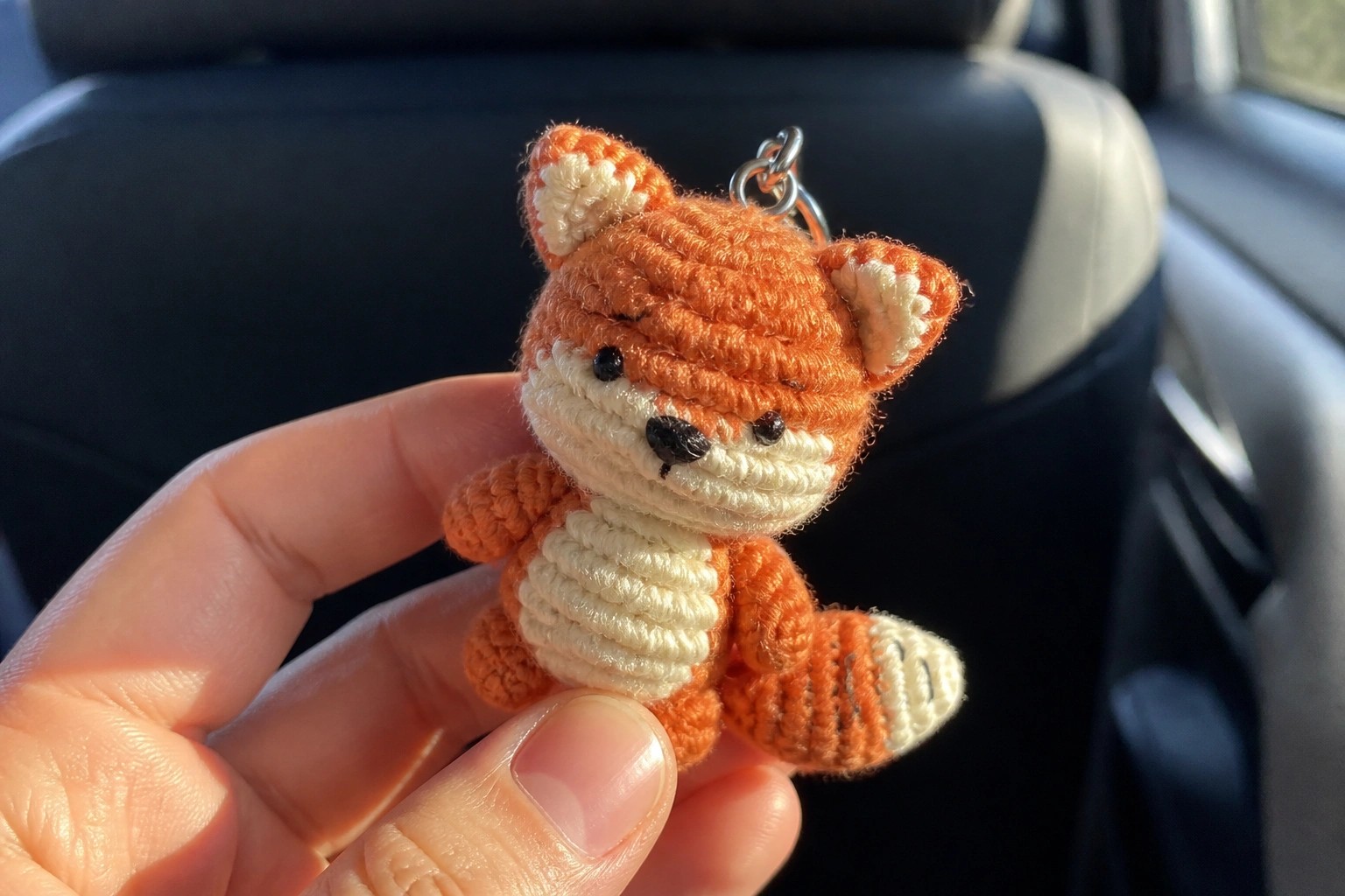 A small crocheted orange fox with white muzzle and belly held between fingers as a keychain.