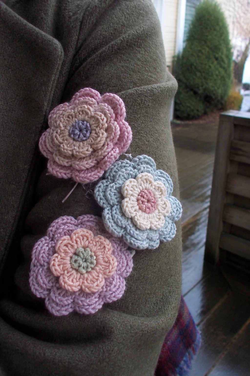 Three pastel crocheted flowers pinned to the shoulder of a green coat