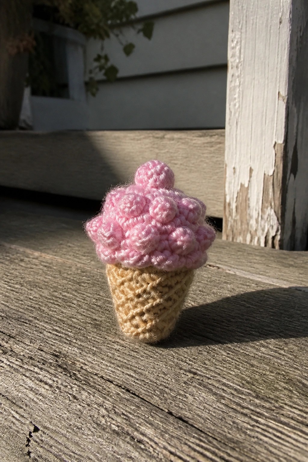 Tiny pink crocheted ice cream cone with beige waffle base on wood.