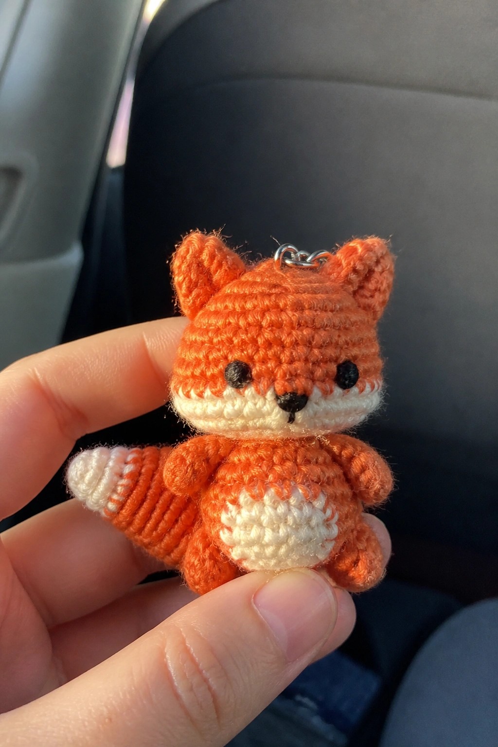 A small crocheted orange fox with white muzzle and belly held between fingers as a keychain.