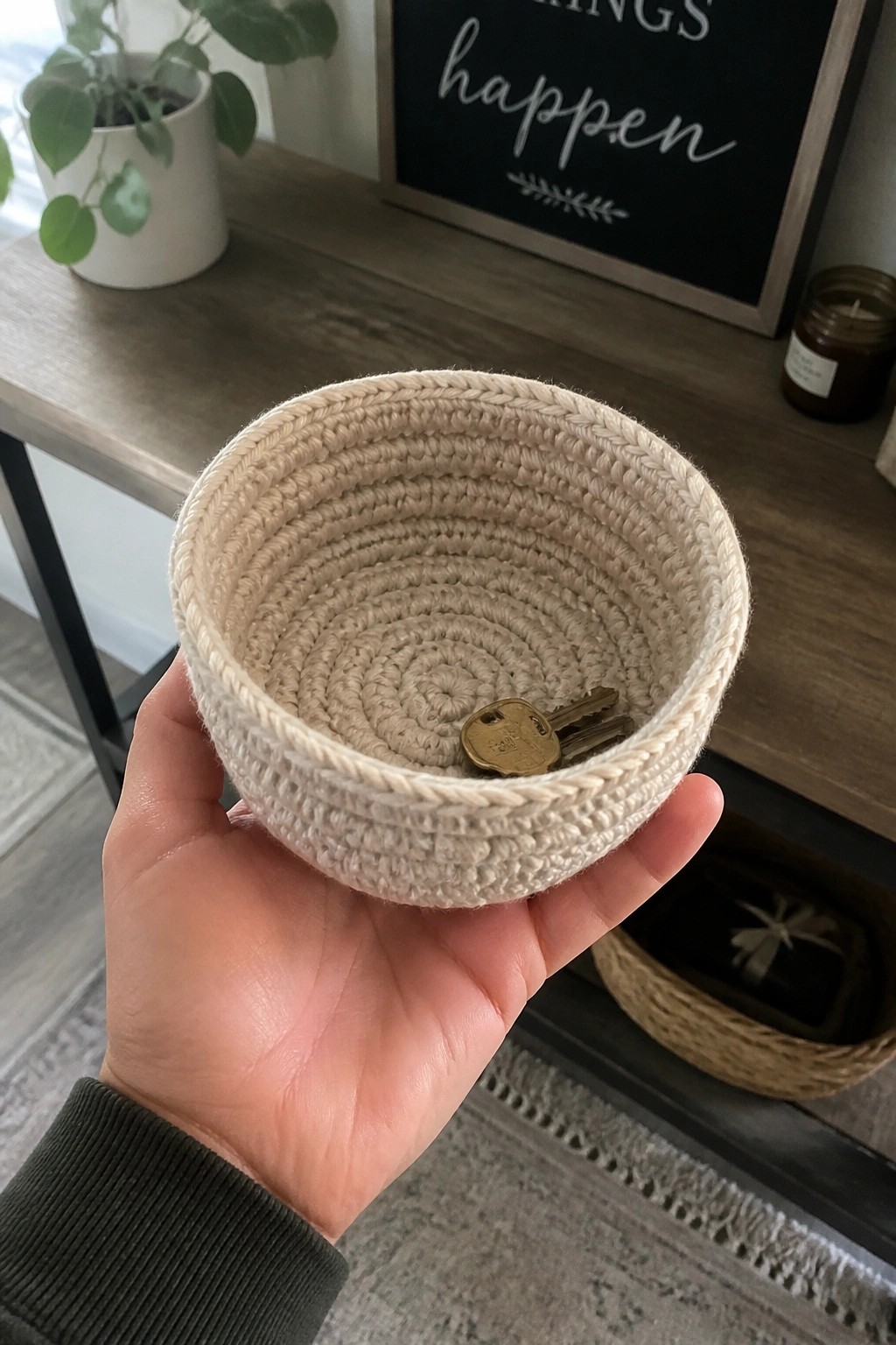 Hand in green sleeve holding beige crocheted basket with keys inside.