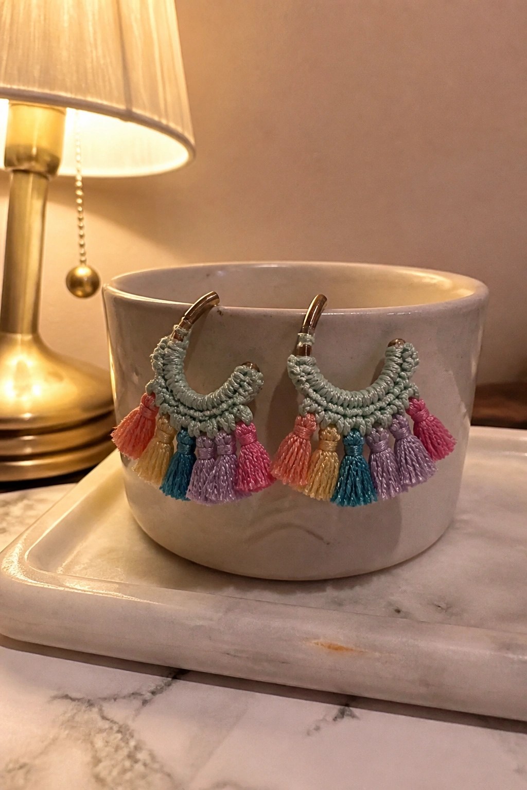Pastel macrame hoop earrings with rainbow tassels on a white bowl