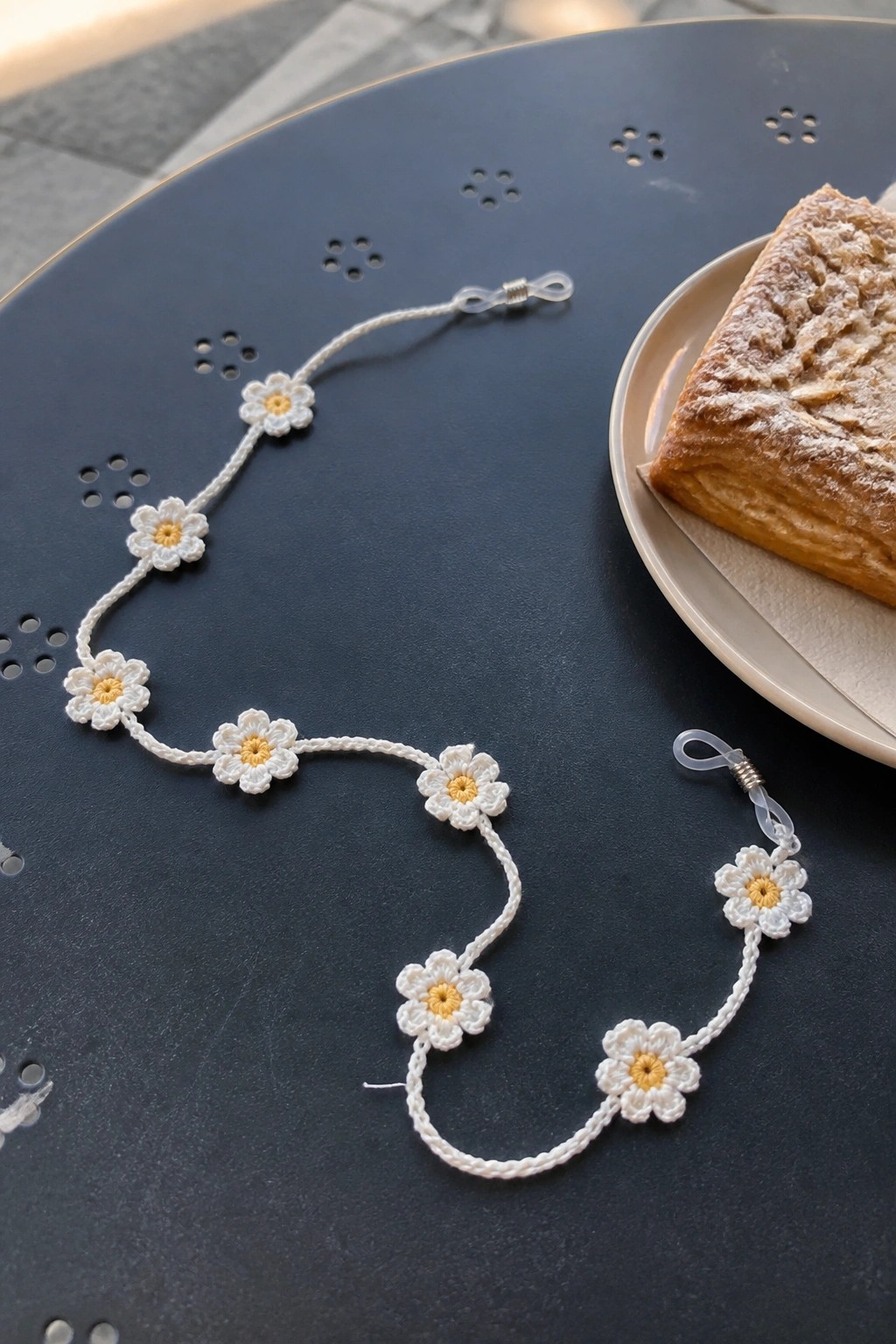 Crocheted daisy chain strap with white flowers and yellow centers beside a pastry.