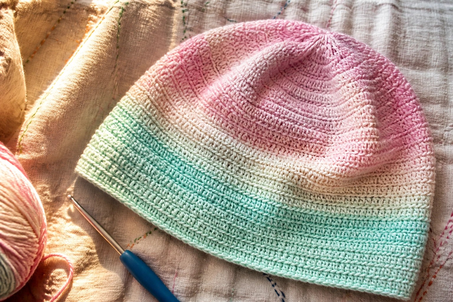 Pastel pink to mint green ombre crochet hat with hook on floral fabric.