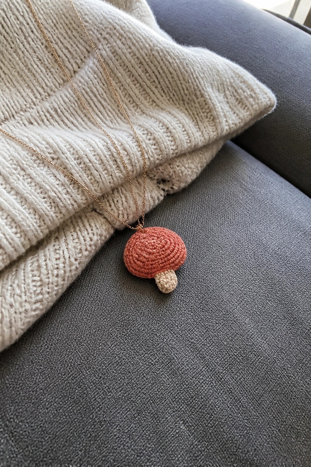 Red crocheted mushroom pendant on gold chain atop white knit sweater