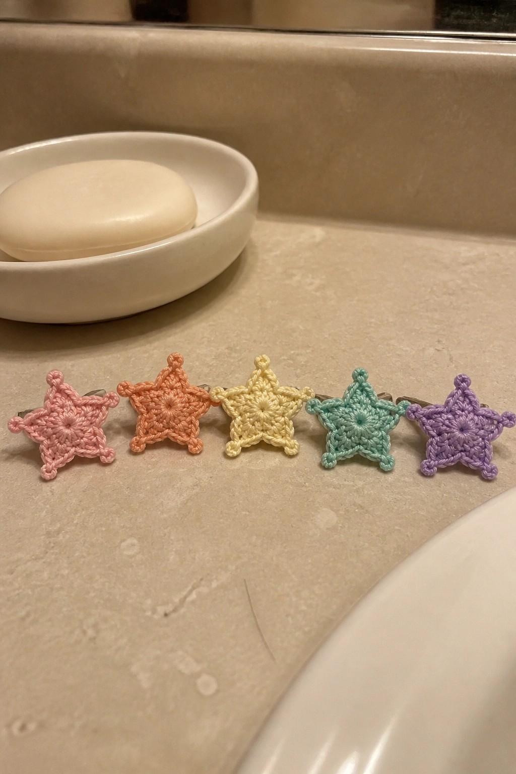 Five colorful crocheted star hair clips lined up on a marble bathroom counter