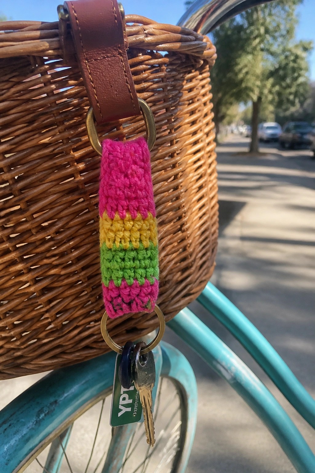 Crocheted pink-yellow-green striped holder with keys on wicker bicycle basket