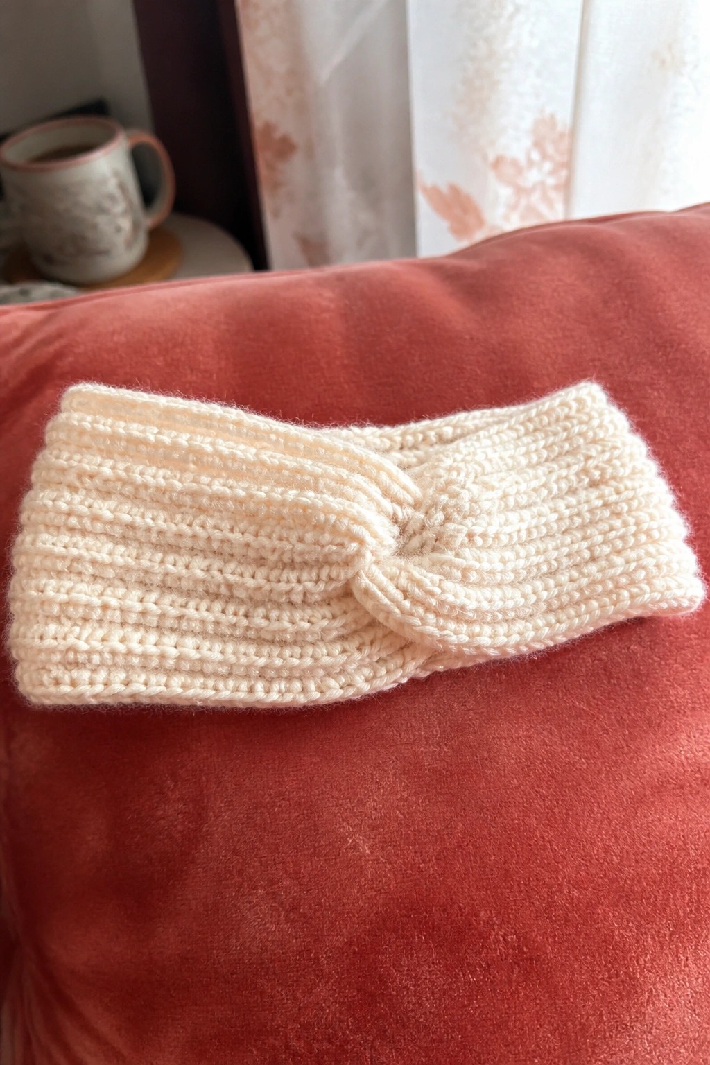 A cream ribbed headband with a center twist lies on red fabric.