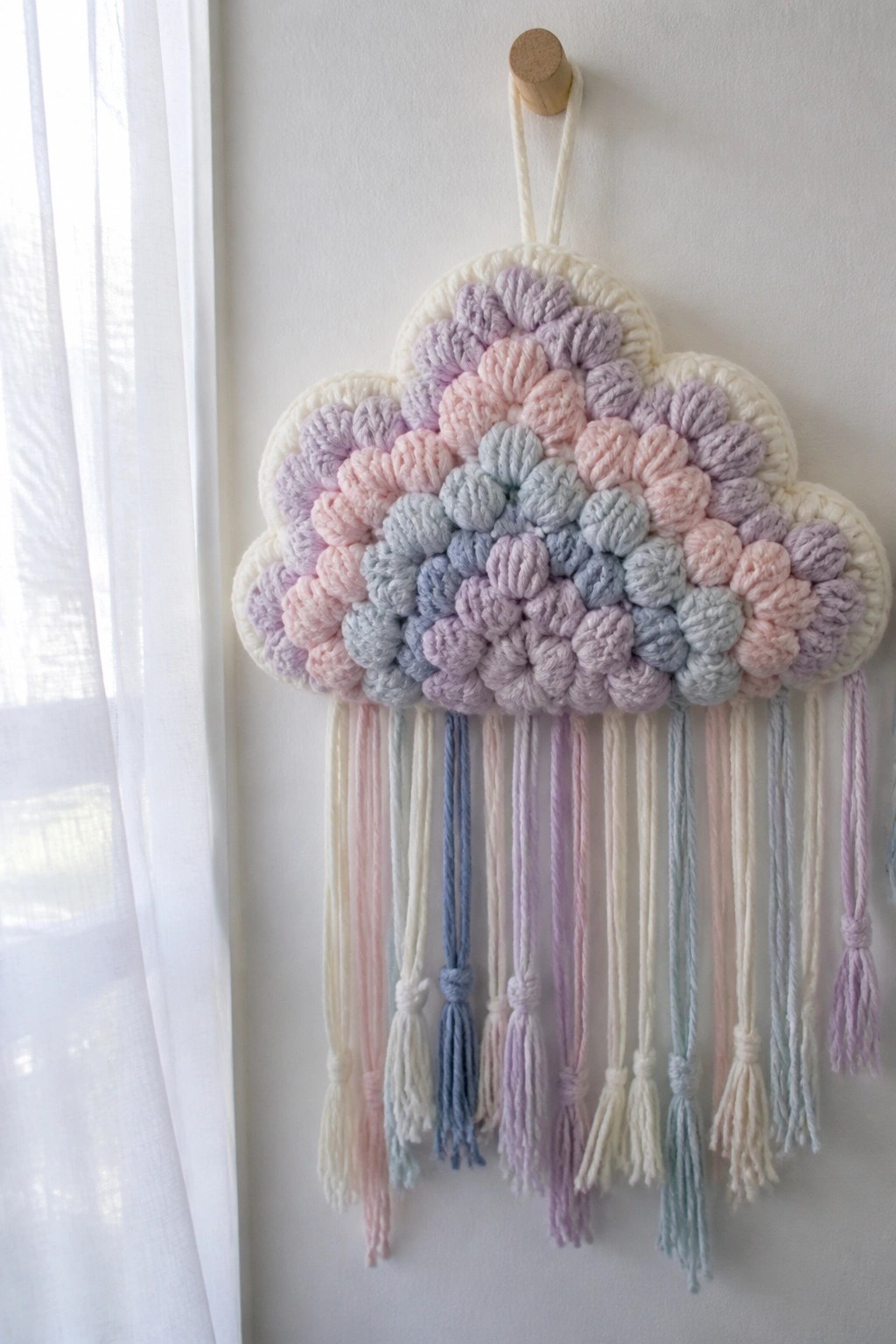 Pastel crocheted cloud wall hanging with colorful yarn tassels on white wall