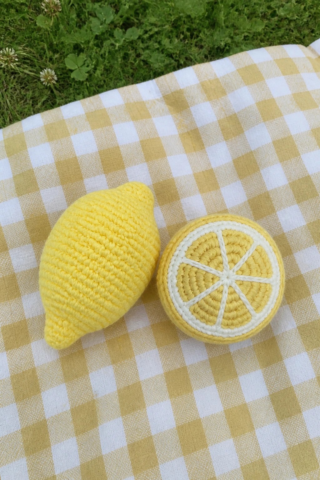 Crocheted yellow lemon and slice on gingham picnic blanket in grass