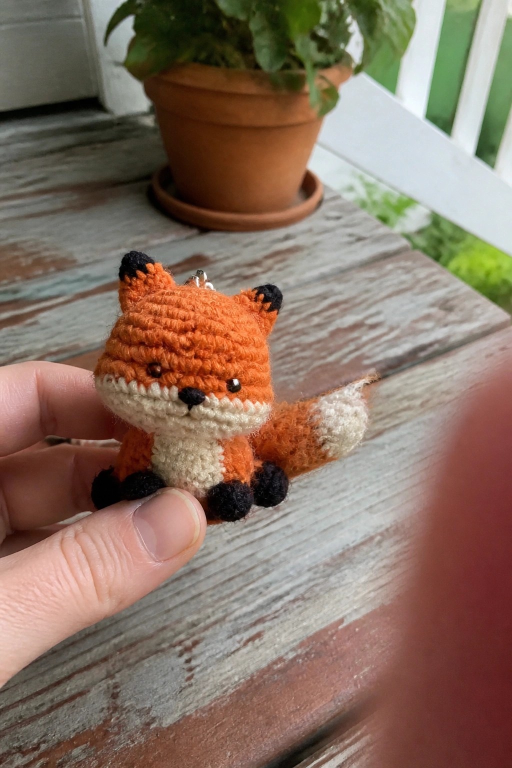 Hand holding small crocheted orange fox with white muzzle and black feet.